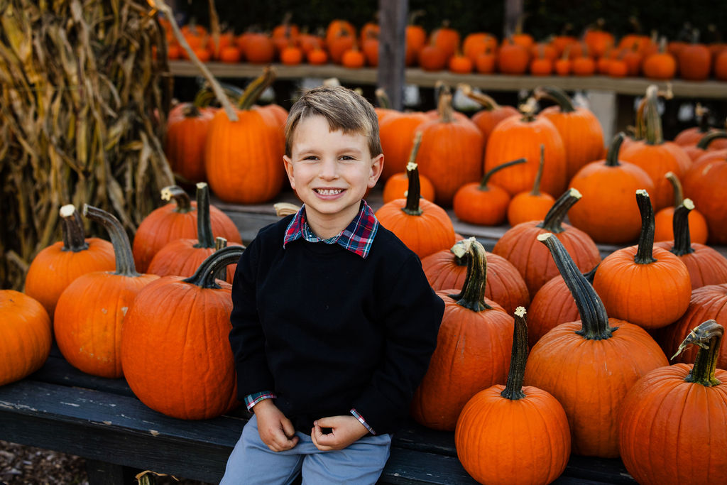 Little boy sits in the pumpkins at The Farmer's Daughter in Kingstown, RI for fall portrait session